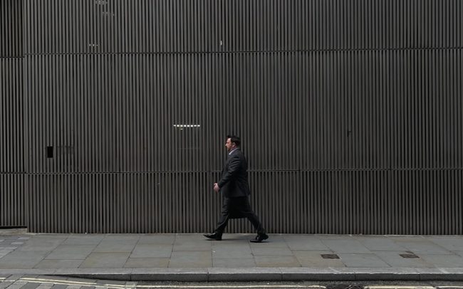 a man walking down a sidewalk next to a tall building